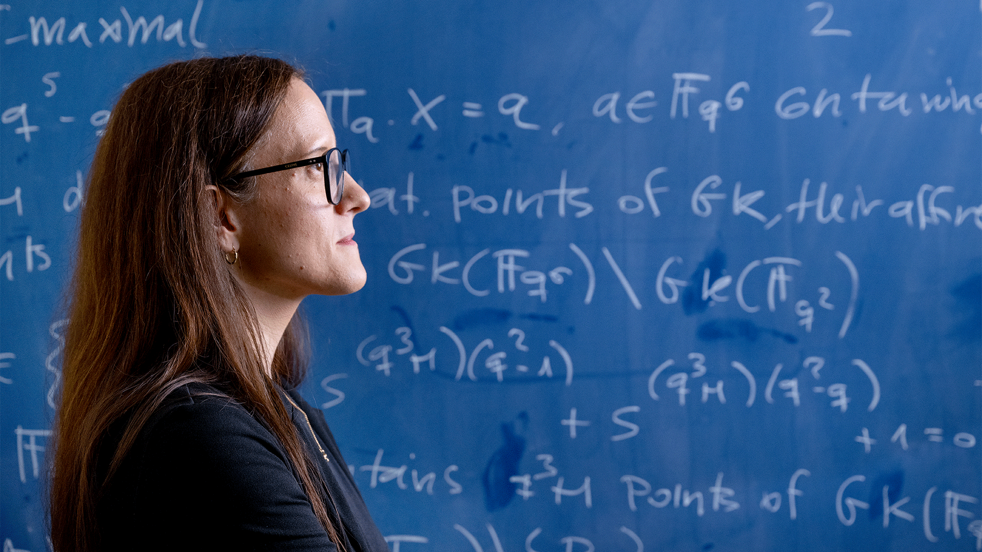 DTU professor Maria Montanucci pictured in profile in front of a blue board filled with mathematical formulas.